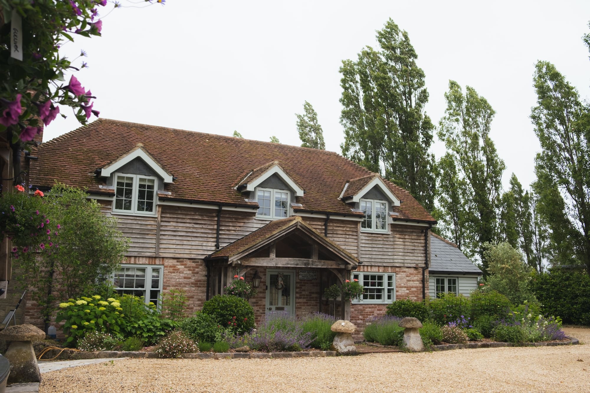 Large rustic home exterior featuring a brick ground floor, wooden siding on the upper level, a timber porch, and a landscaped front garden with stone mushroom ornaments.